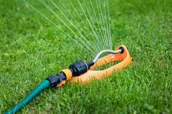 Полив газона - разбрызгиватель воды работает в зеленой траве дома b — стоковое фото