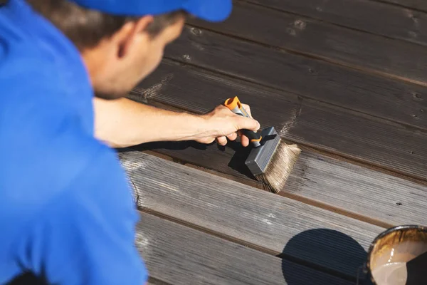 Hombre pintando tablones de madera terraza con aceite de protección de madera — Foto de Stock