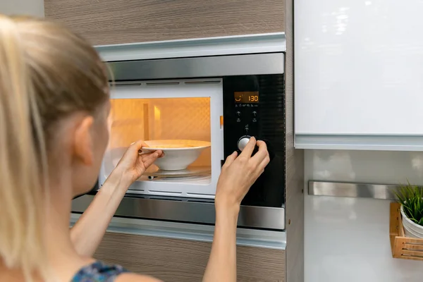 Mujer caliente la comida en el horno de microondas en casa —  Fotos de Stock