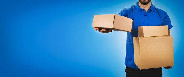 delivery service man holding cardboard boxes on blue background 