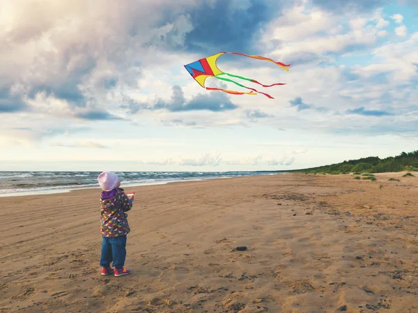 Klein meisje vliegen een vlieger op het strand bij zonsondergang — Stockfoto