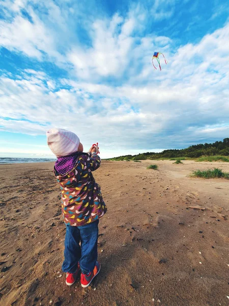 Klein kind vliegt een vlieger in de lucht op het strand op winderige lachen — Stockfoto