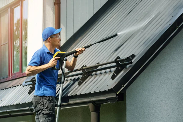 Mann steht auf Leiter und reinigt Hausdach mit Hochdruckreiniger Stockbild