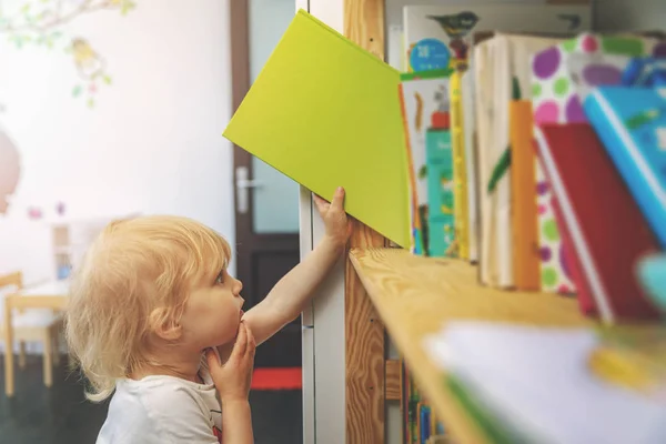 Petite fille choisir et prendre livre de l'étagère à lire — Photo