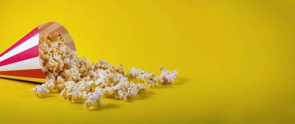 Bolsa de cono rayado con palomitas de maíz derramadas sobre fondo amarillo con Fotos de stock