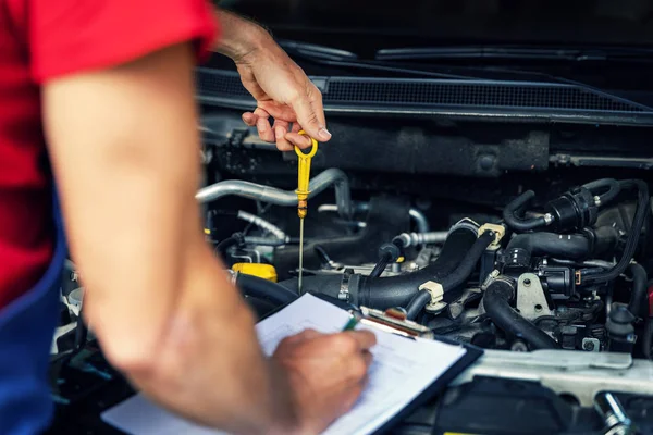 car inspection and maintenance - mechanic check engine oil level and writing in checklist