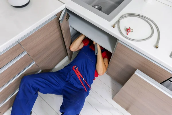 Loodgieter werken onder binnenlandse keuken gootsteen, het repareren van waterleidingen — Stockfoto