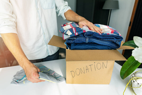 благотворительность - человек дома кладет одежду в картонную коробку для доны
