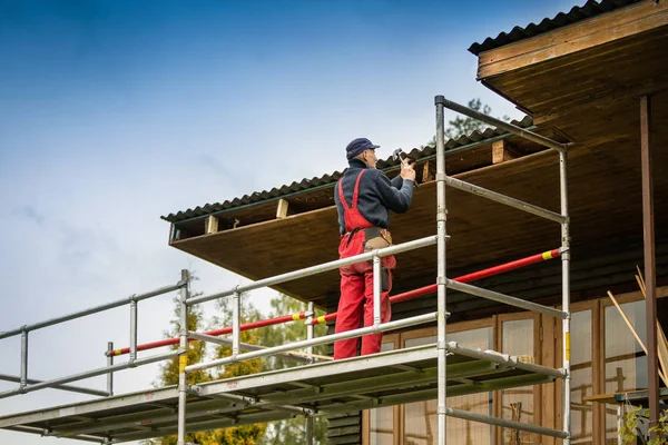 Mann steht auf Baugerüst und restauriert altes Holzhausdach — Stockfoto