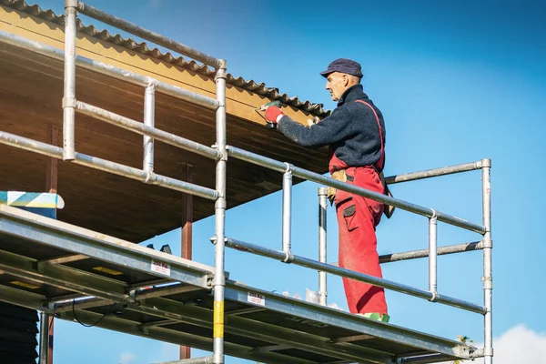 Человек на строительных лесах устанавливает новые деревянные доски на крыше дома ea — стоковое фото