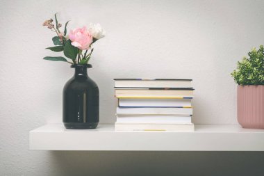 Kitaplar ve saksılarla dolu beyaz bir duvarda.