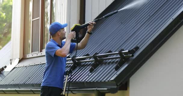 はしごに立って高圧洗浄機で金属製の屋根を掃除する男 — ストック動画