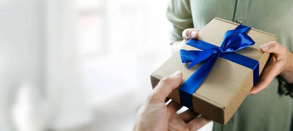 hand giving gift box with blue ribbon to a woman. copy space