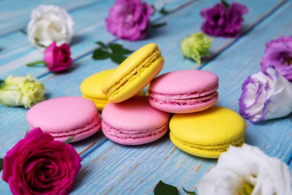 pink and yellow macarons with flowers on blue wooden table