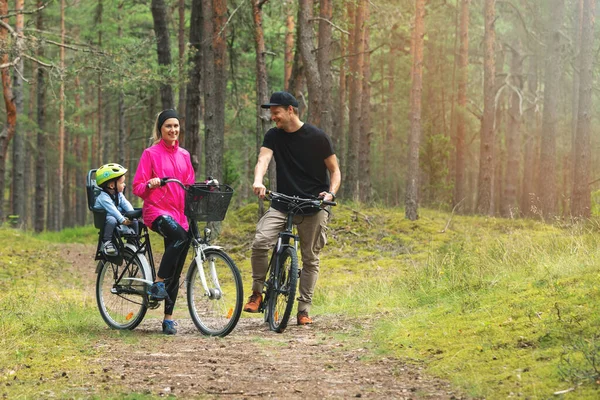 年轻的家庭骑自行车在森林小径上与孩子在自行车儿童座位 积极参加户外运动 — 图库照片