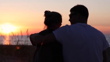 Genç aşıklar kumsalda romantik altın gün batımında oturuyorlar. kule görüntüsü