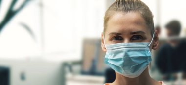 Ofisteki yüz maskesi takan genç bir kadın. Virüs salgını sırasında sosyal uzaklık ve güvenlik. Boşluğu kopyala