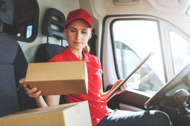 Kırmızı üniformalı bayan teslimatçı minibüste oturuyor ve paketlerle çalışıyor.