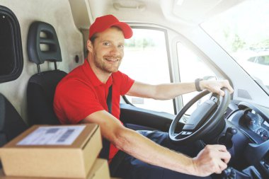 Kırmızı üniformalı gülümseyen teslimatçı minibüs sürücüsü ve paket teslimatı.