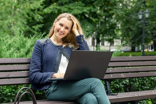 在城市公园的长椅上 年轻迷人的微笑的女人拿着笔记本电脑放松一下 — 图库照片