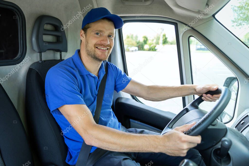 transportation services - young male driver in blue uniform driving a van. smiling at camera