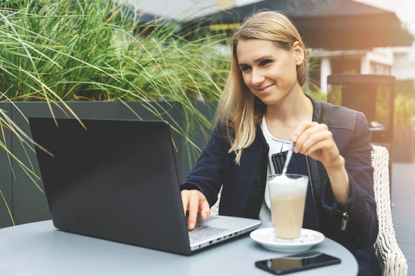 年轻妇女在户外的咖啡厅平台上喝咖啡拿铁 并使用笔记本电脑 自由应聘的远程工作 — 图库照片