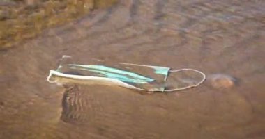 Tıbbi yüz maskesi suda yüzüyor. Okyanus kirliliği. Coronavirüs sonuçları