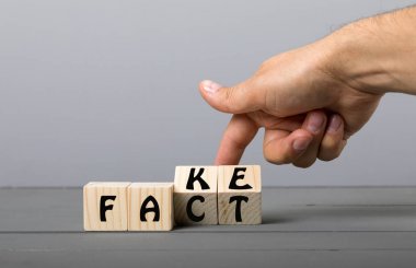 Gerçek veya Fake kavramı, el Flip ahşap küp gri arka planda kelime değiştirmek.