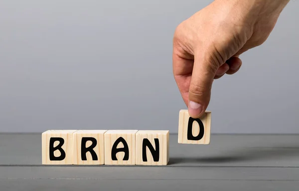 Hand of male putting wood cube block with word BRAND on grey wooden table