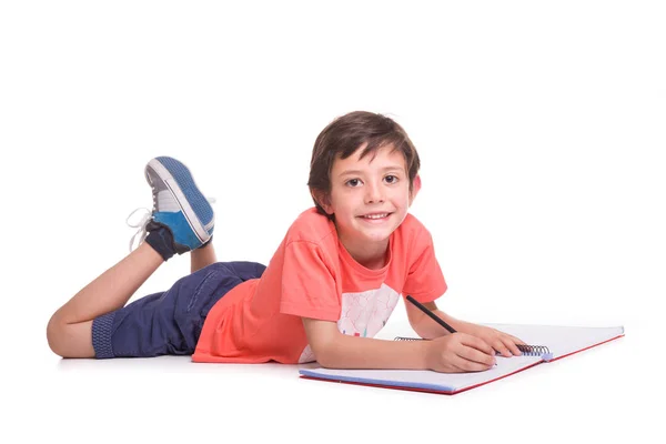 Niño de la escuela feliz acostado en el suelo y dibujando con lápiz, aislar Imagen De Stock