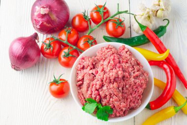 Bir beyaz plaka ve taze domates, biber, soğan, sarımsak rustik masa yakın çekim üzerinde çiğ kıyılmış domuz. üstten görünüm