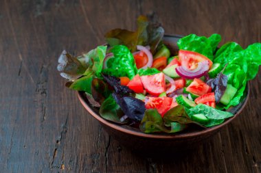 Karışık yeşil taze yeşil salata yaprakları, domates, soğan ve koyu ahşap masa üzerinde salatalık. Yeme temiz ve Diyet yemekleri.