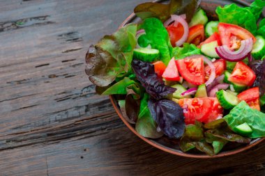Karışık yeşil taze yeşil salata yaprakları, domates, soğan ve koyu ahşap masa üzerinde salatalık. Yeme temiz ve Diyet yemekleri.