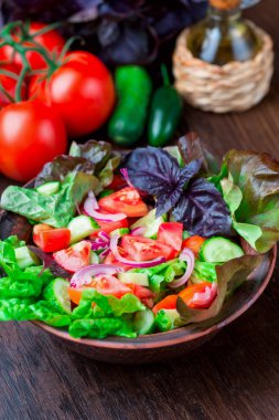Karışık yeşil taze yeşil salata yaprakları, domates, soğan ve koyu ahşap masa üzerinde salatalık. Yeme temiz ve Diyet yemekleri.