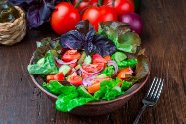 Karışık yeşil taze yeşil salata yaprakları, domates, soğan ve koyu ahşap masa üzerinde salatalık. Yeme temiz ve Diyet yemekleri.