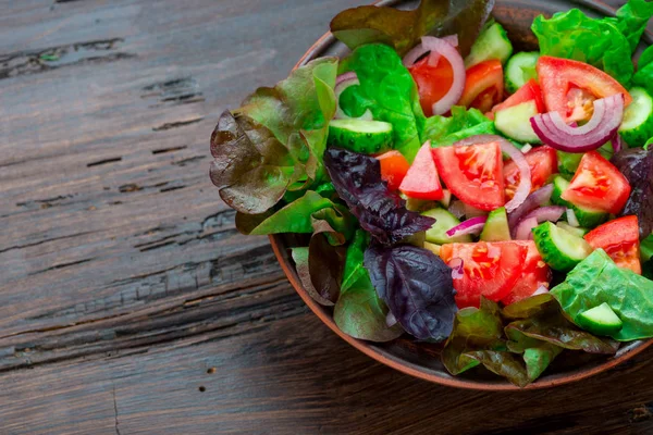 Karışık yeşil taze yeşil salata yaprakları, domates, soğan ve koyu ahşap masa üzerinde salatalık. Yeme temiz ve Diyet yemekleri.