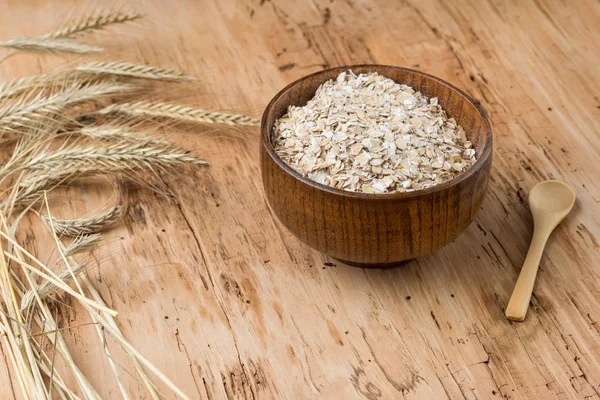 Rolled oats or oat flakes in bowl with wooden spoons, golden wheat ears rustic wooden background. Healthy lifestyle, healthy eating concept