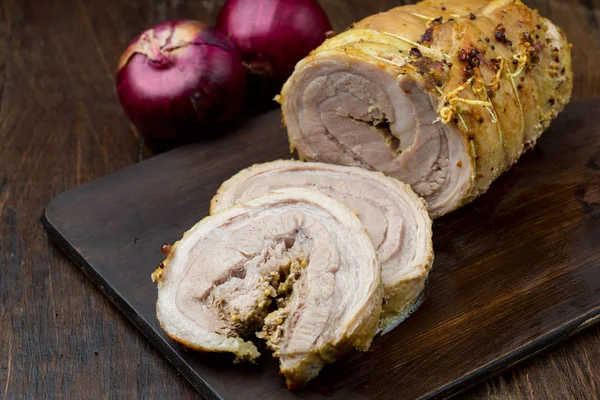 Roasted Pork shoulder cut on slices on chopping board on white peeling paint boards with garlic.