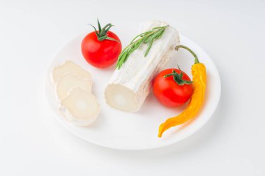 Kiraz domates ve biberiye yaprağı beyaz masa üzerinde keçi peyniri beyaz seramik tabağa dilimlenmiş, ön görünüm