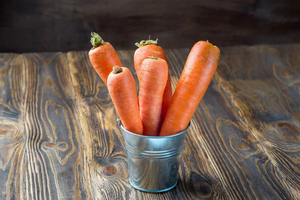 Fresh carrot in the metal bucket isolated on rustic wooden table — Stock Photo, Image