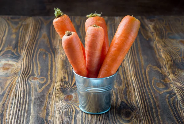 Fresh carrot in the metal bucket isolated on rustic wooden table — Stock Photo, Image