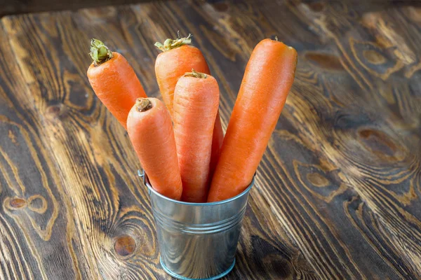 Fresh carrot in the metal bucket isolated on rustic wooden table — Stock Photo, Image