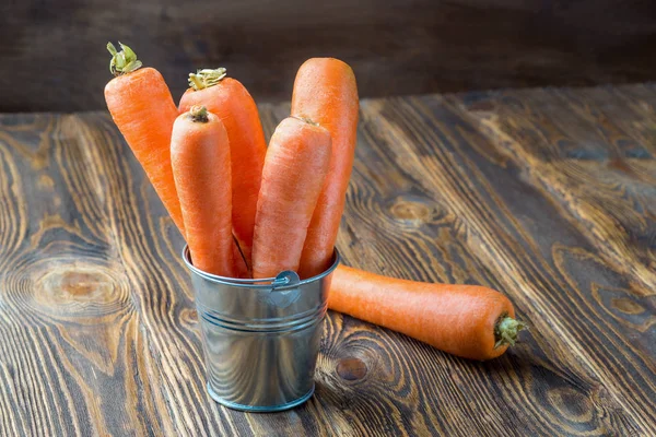 Fresh carrot in the metal bucket isolated on rustic wooden table — Stock Photo, Image