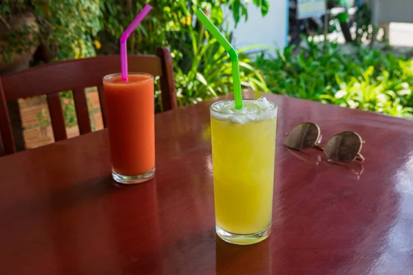 Twee glazen fruit smoothie, ananas en tomaten op een rode ta — Stockfoto