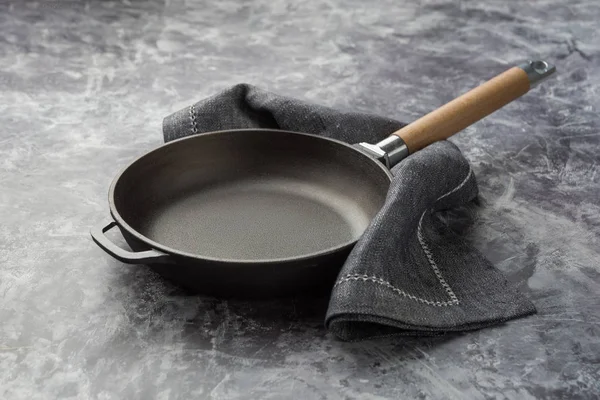 Empty cast iron frying pan on dark grey culinary background.