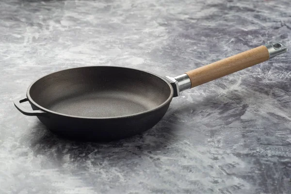 Empty cast iron frying pan on dark grey background.