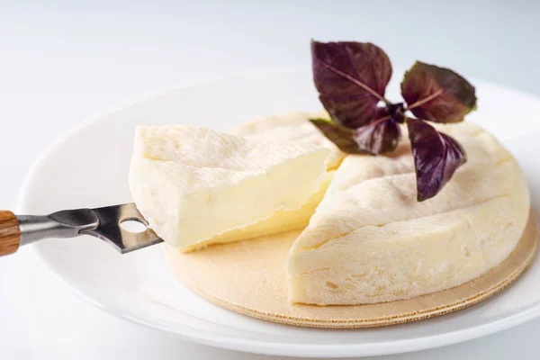 Brie fresco e una fetta su un tagliere di legno con basilico fresco — Foto Stock