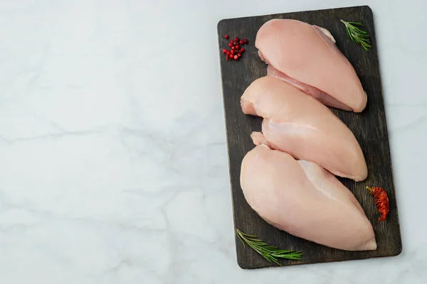 Raw chicken fillets on dark wooden board