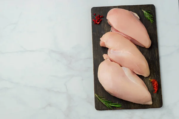 Raw chicken fillets on dark wooden board
