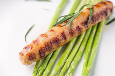 Beyaz tabakta kuşkonmaz ile kızarmış sosis, ahşap masa.